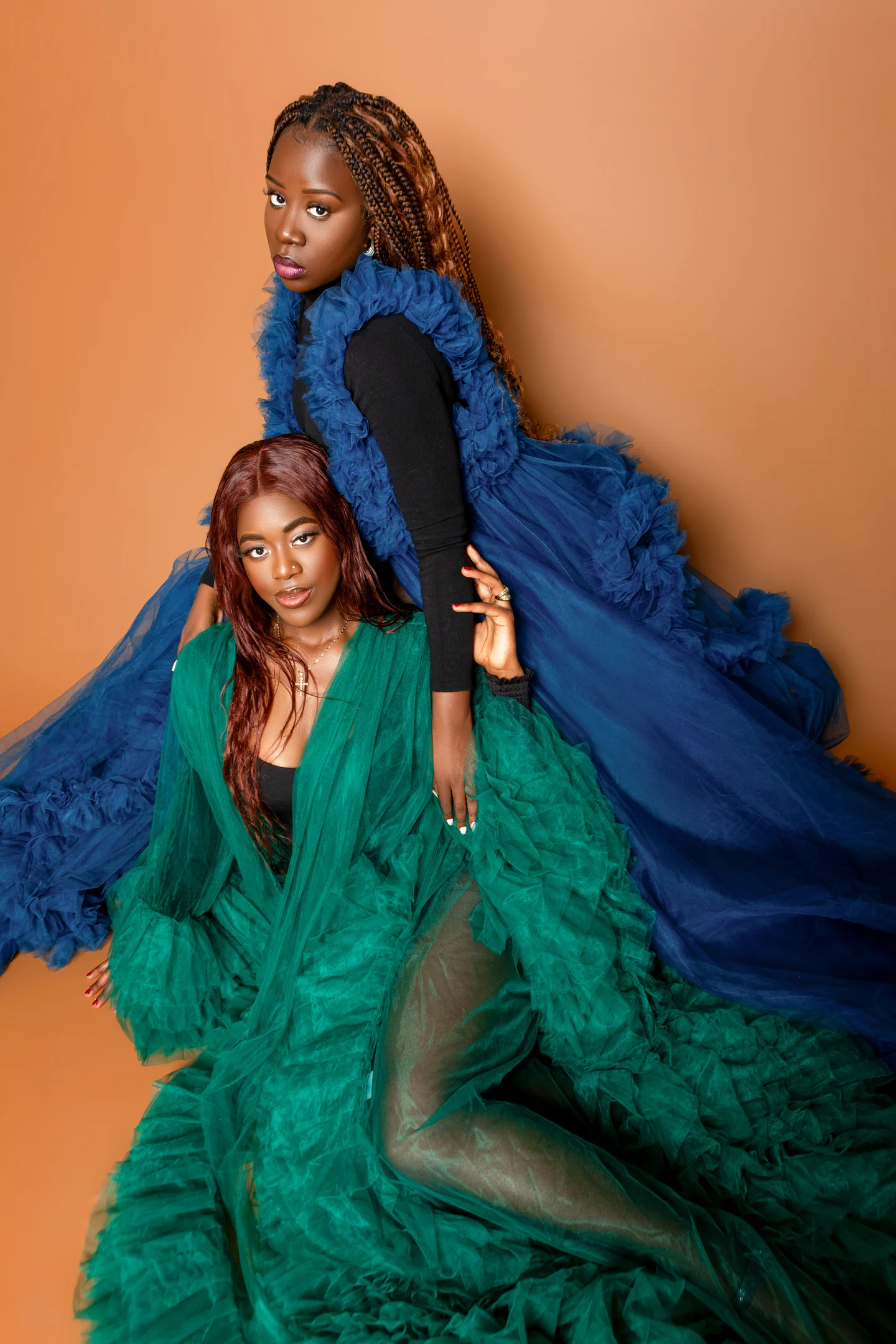 Deux femmes en robes à volants bleue et verte posent à des hauteurs différentes sur un fond ocre.