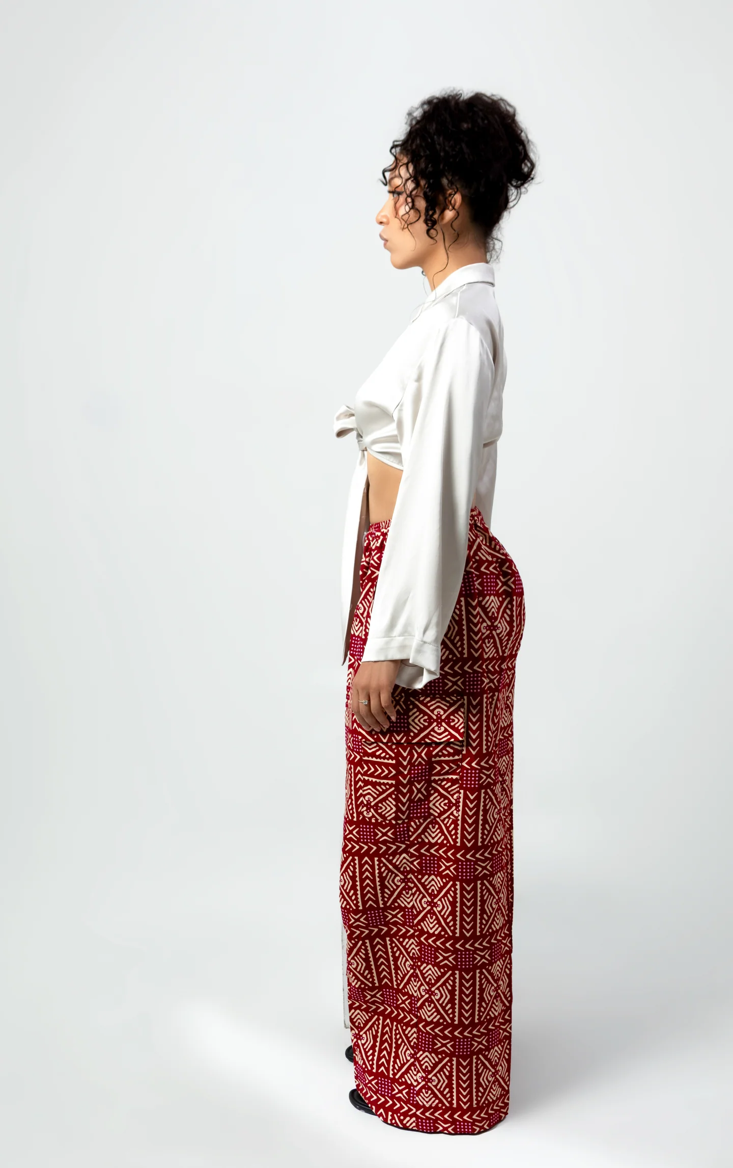 Portrait de mode de profil, avec un chemisier blanc noué et un pantalon à motifs rouges.