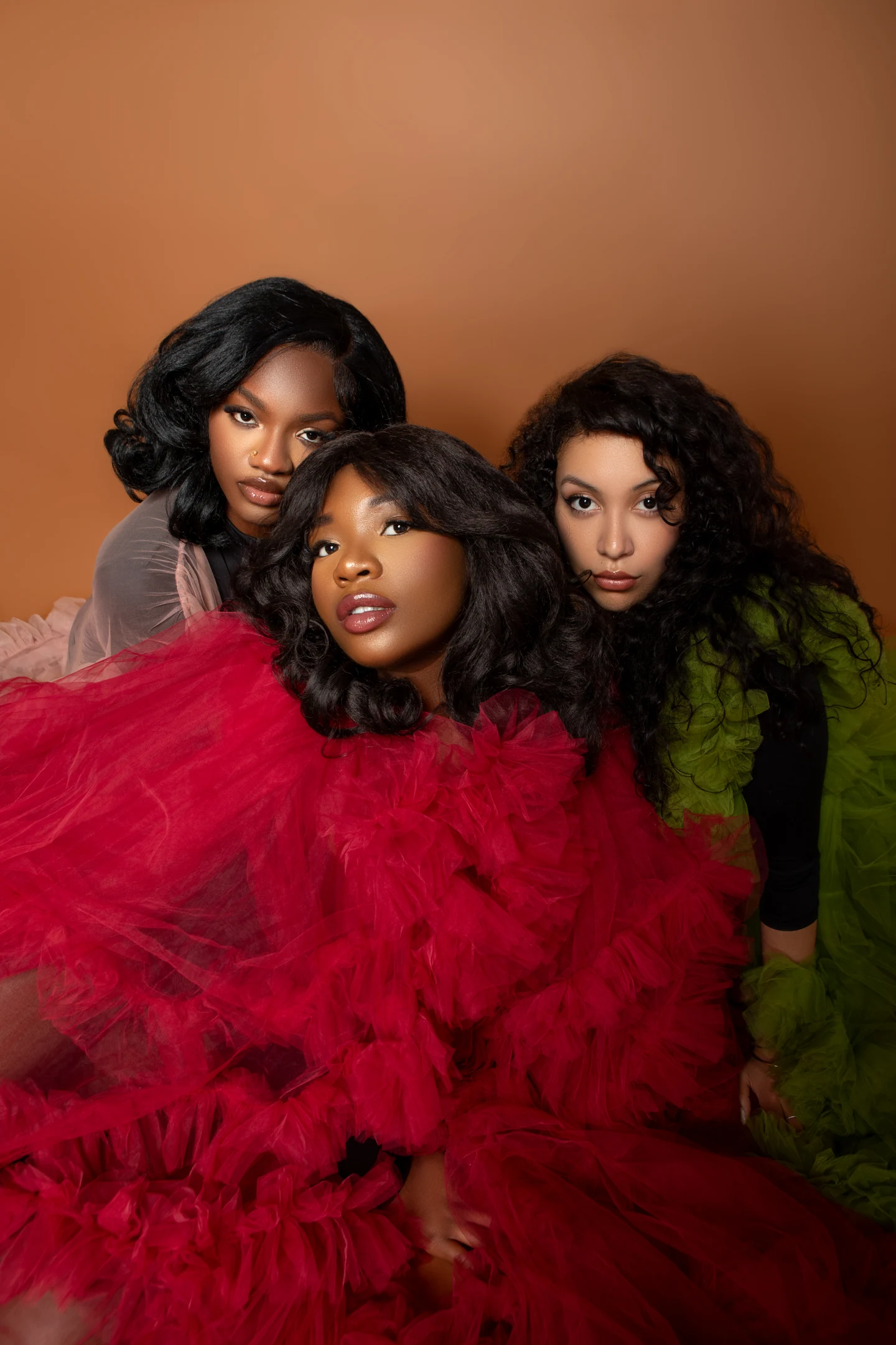 Trois femmes dans une composition éditoriale en rouge, rose et vert olive sur un fond ocre.