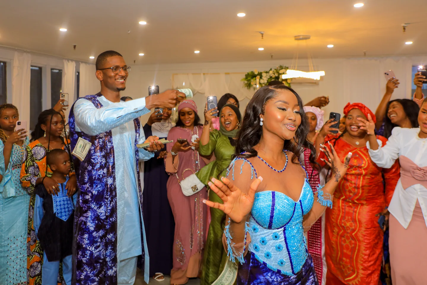 Femme et homme en tenues bleues pendant une danse de réception, entourés d’invités qui sourient.