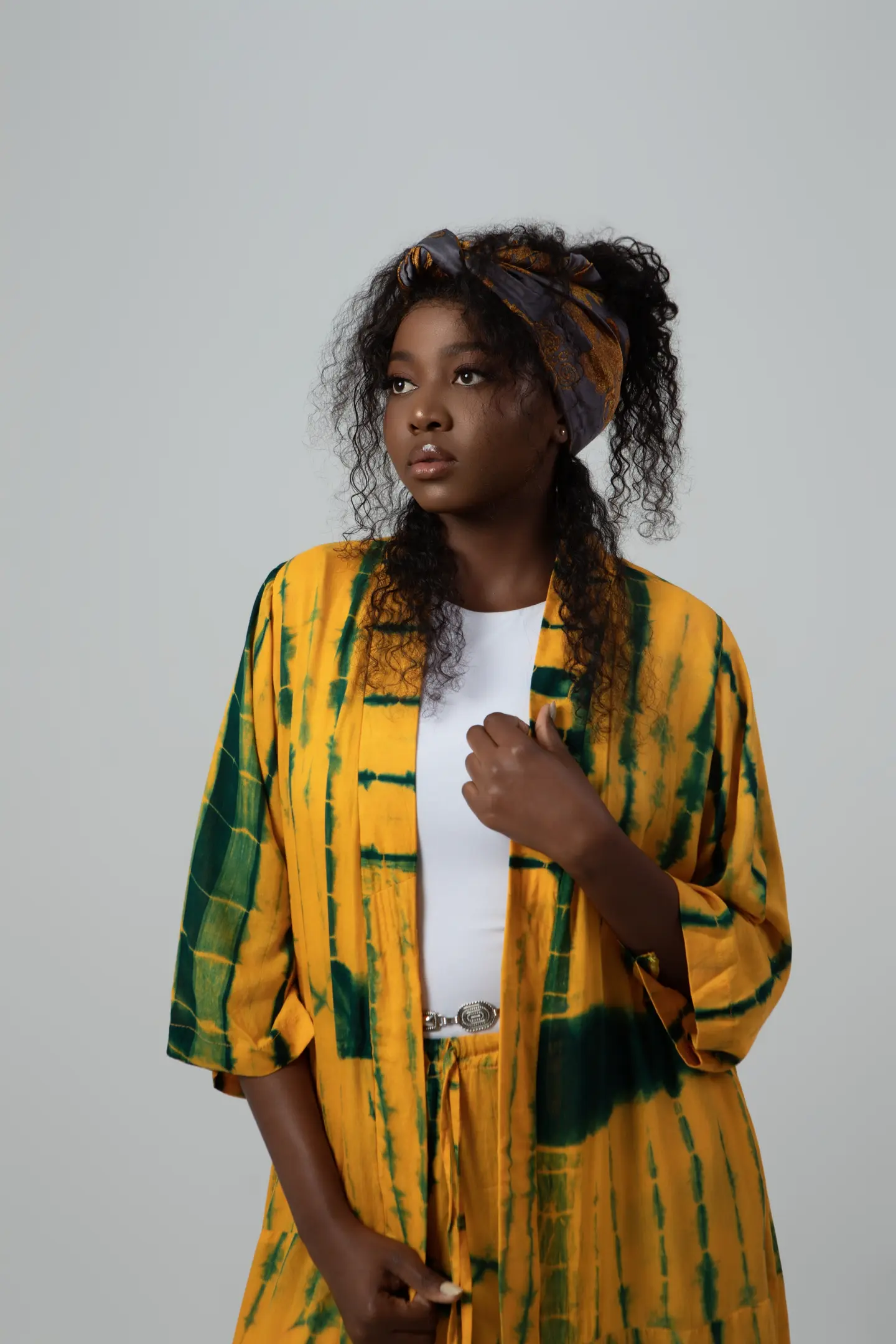 Portrait d’une femme portant une veste à motifs jaunes et verts, sur un fond gris clair.