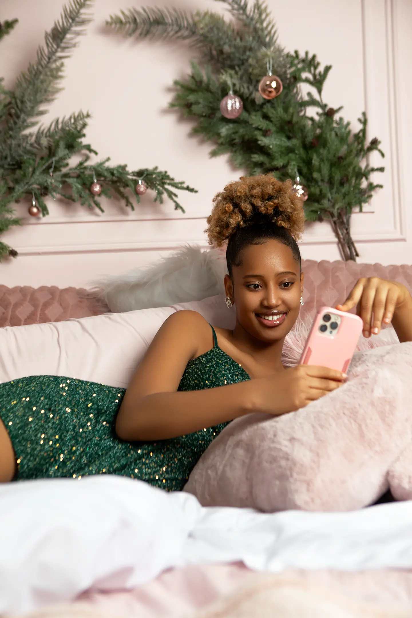 Femme souriante allongée sur un lit, dans un décor chaleureux avec un sapin de Noël.