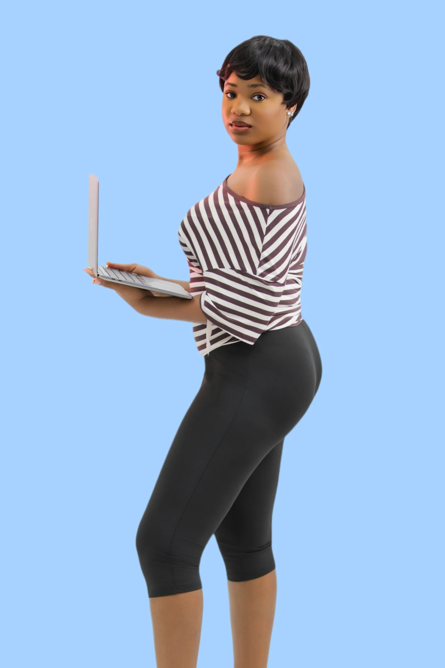 Femme aux cheveux courts en haut rayé, tenant un ordinateur portable ouvert, sur fond bleu.