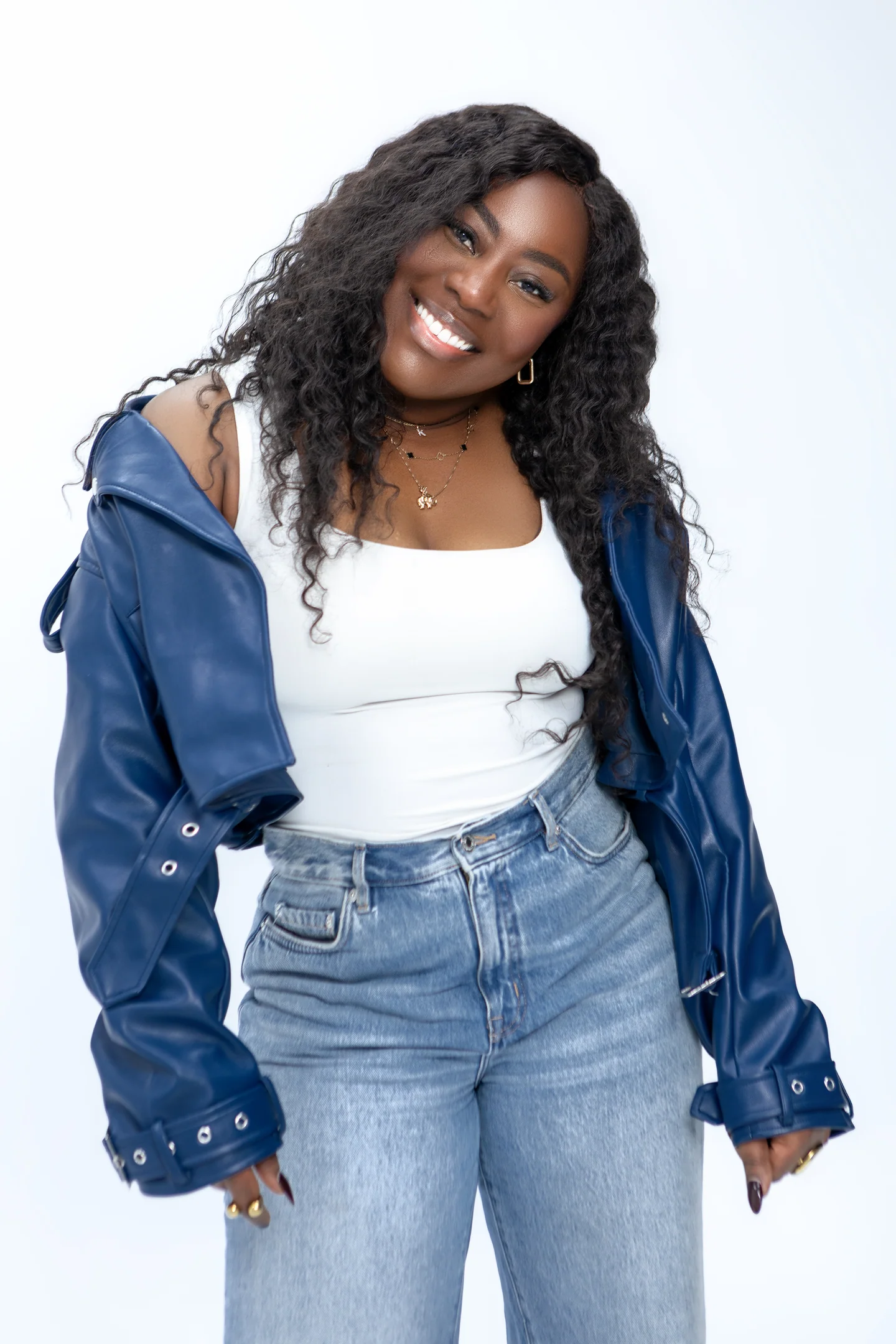 Femme souriante en veste bleue, haut blanc et jean, la tête légèrement inclinée sur fond clair.