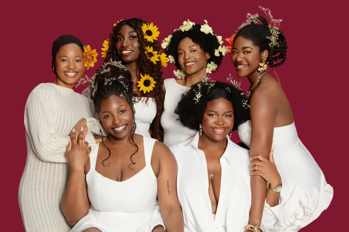 Six femmes en tenues blanches et coiffures fleuries réunies pour un portrait de groupe sur un fond bordeaux.
