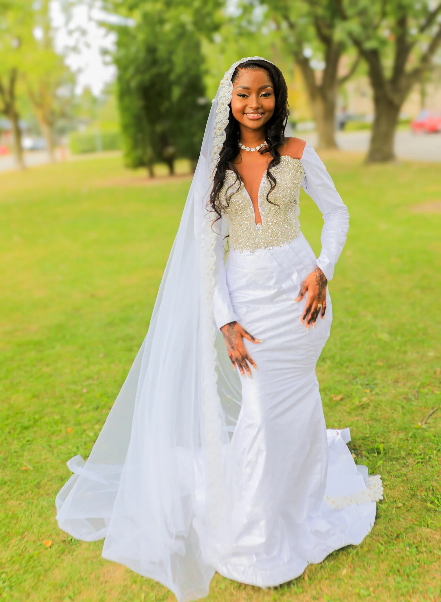 Portrait en pied d’une mariée en robe et voile blancs, debout sur une pelouse.