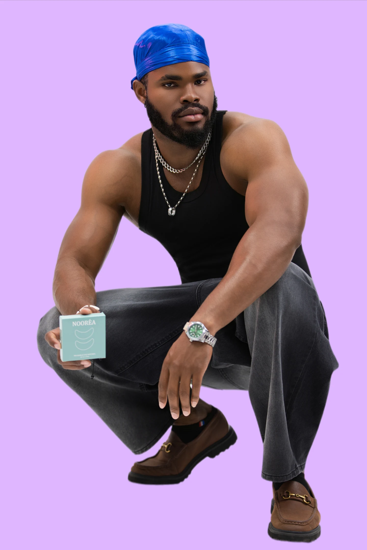 Un homme en débardeur noir et durag bleu présente une boîte de soin sur un fond violet.