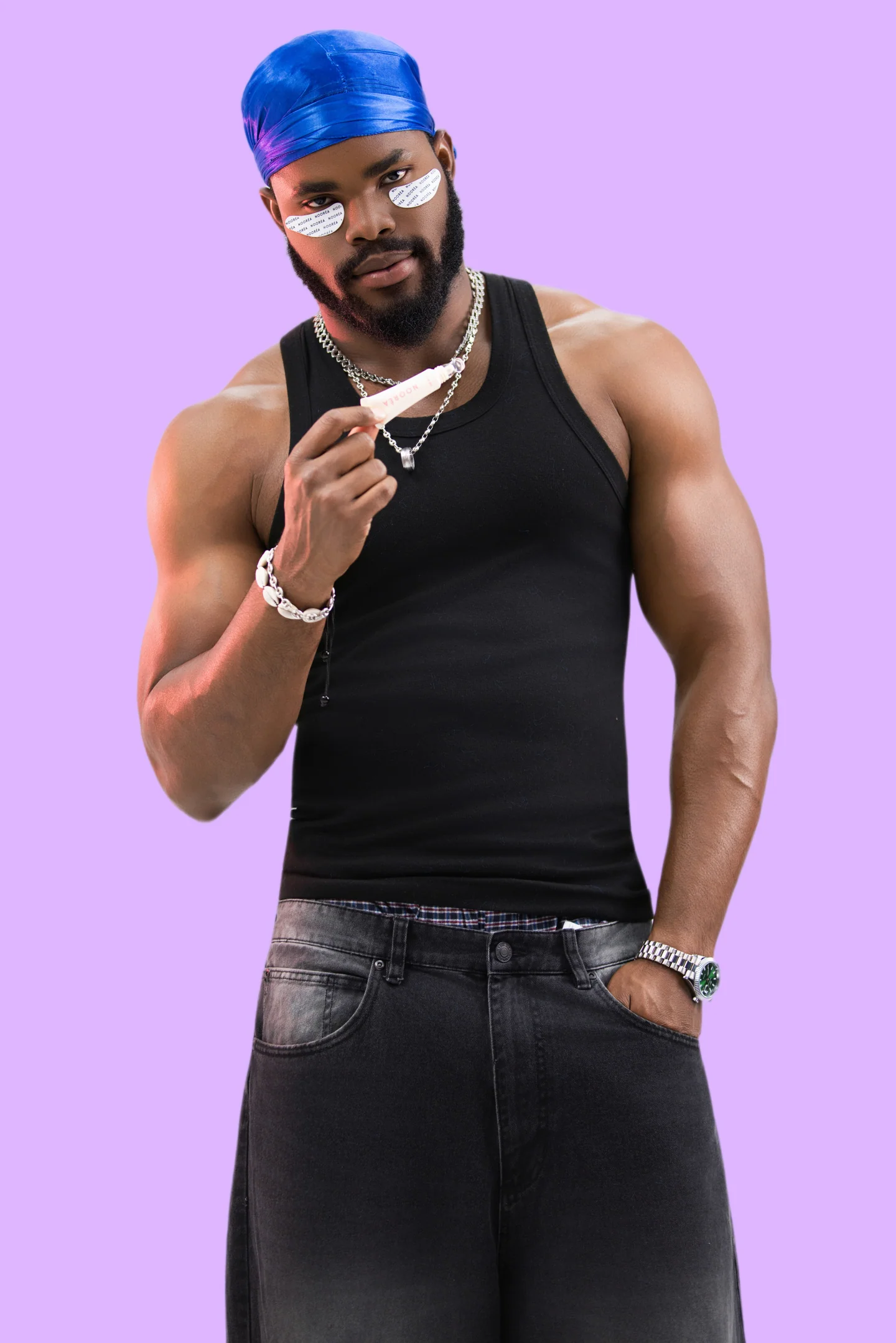 Homme en durag bleu et débardeur noir, avec des patchs sous les yeux, tenant un patch devant lui sur fond violet.